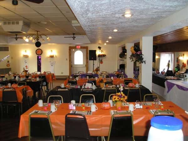 Dining hall with tables set for Halloween in orange linen, tables decorated with pumpkins and and fall flowers and balloons and flower decorations on the wall