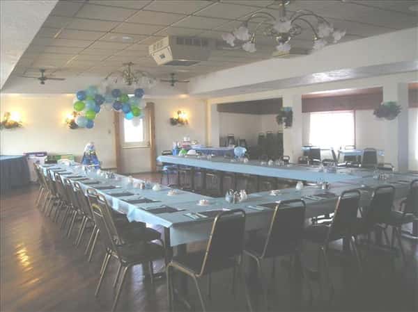 Event room with tables in light blue linen set for a special occasion and decorated with blue and green balloons