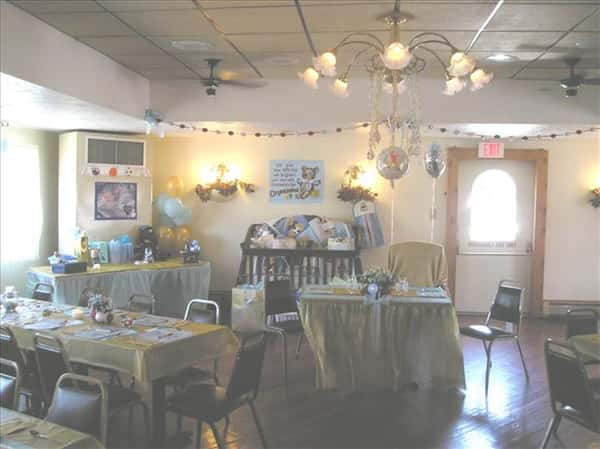 Event room decorated for a baby shower with colorful tables set for a party, a buffet table covered with presents and a baby cot in the background decorated with colorful presents