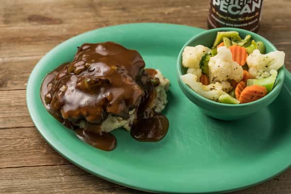 Mashed potatoes topped with brown gravy with a bowl of vegetables