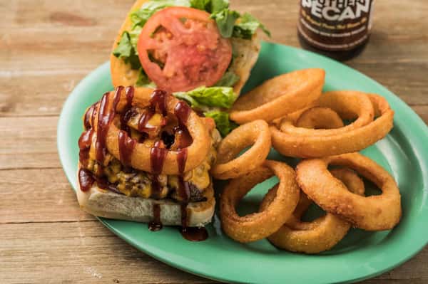 Cheeseburger topped with an onion ring, tomato, letttuce and barbecue sauce with a side of onion rings