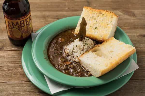 A bowl of stew with two pieces of garlic bread