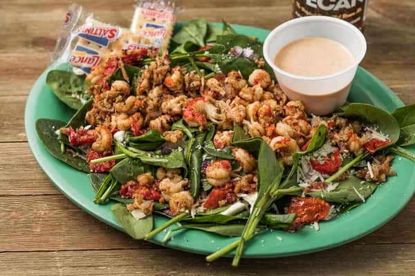 A spinach salad with shrimp, shredded cheese and red sauce marinara sauce