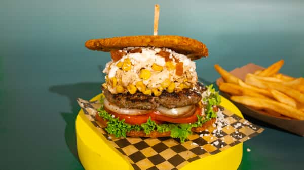 Burger on a plantain base, 100% handmade beef patty, shredded chicken in sauce, grilled corn, shredded cheese, lettuce, tomato, and grilled onions. Apto sauce and pineapple sauce. ALL OUR BURGERS AND HOT DOG ARE SERVED WITH FRIES! Hamburguesa sobre una base de plátano, carne de res 100% artesanal, pollo desmechado en salsa, maíz a la parrilla, queso rallado, lechuga, tomate y cebolla a la parrilla. Salsa Apto y salsa de piña. VIENE CON PAPAS A LA FRANCESA INCLUIDAS