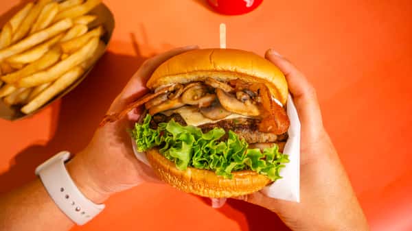 The Capital. Brioche bun, 100% handmade beef patty, garlic mushrooms, smoked bacon, cheese, lettuce, tomato, and grilled onions. Apto sauce and pineapple sauce. ALL OUR BURGERS AND HOT DOG ARE SERVED WITH FRIES! La Capital - Pan brioche, carne de res 100% artesanal, champiñones al ajo, tocino ahumado, queso, lechuga, tomate y cebolla a la parrilla. Salsa Apto y salsa de piña. TODAS NUESTRAS BURGERS Y PERROS VIENEN CON PAPAS A LA FRANCESA INCLUIDAS