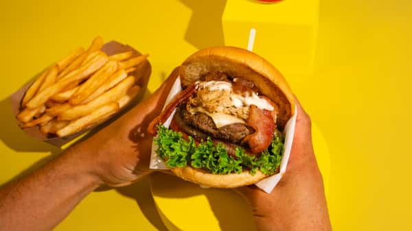 Our signature, the Bumanguesa. Brioche bun, 100% handmade beef patty, shredded chicken in sauce, smoked bacon, cheese, lettuce, tomato, and grilled onion. House sauce and pineapple sauce. ALL OUR BURGERS AND HOT DOG ARE SERVED WITH FRIES! La nuestra, la Bumanguesa. Pan brioche, carne artesanal 100%, pollo desmechado en salsa, tocineta ahumada, queso , lechuga, tomate y cebolla grillé. salsa del apto y salsa de piña. TODAS NUESTRAS BURGERS Y PERROS VIENEN CON PAPAS A LA FRANCESA INCLUIDAS