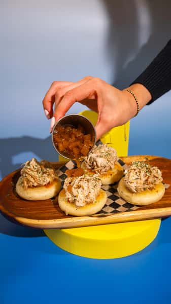 Cheese-filled arepitas topped with shredded chicken in sauce. (x4) 4 arepitas rellenas de queso, con pollito en salsa.