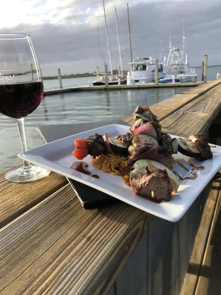 skewers of meat, onion, glass of red wine, overlooking water