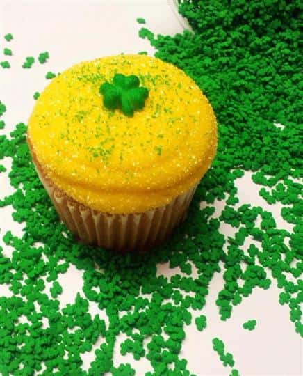 A cupcake with yellow frosting and a green clover on top
