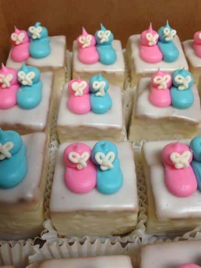 White mini cakes topped with a pink and a blue sugar baby shoe