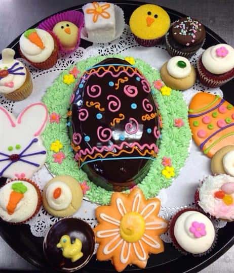 Platter with a chocolate easter egg surrounded of several colorful cookies and cupcakes