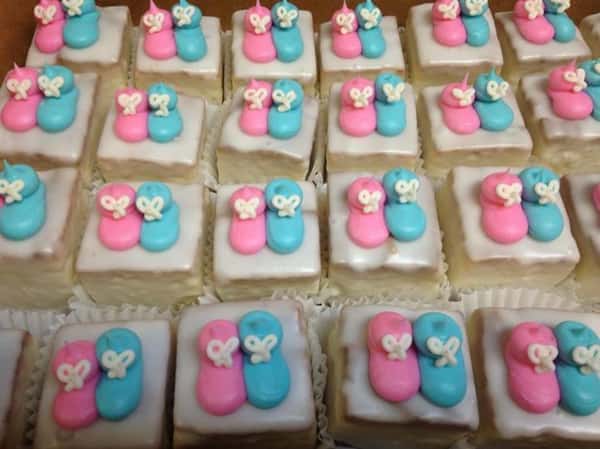 White mini cakes topped with a pink and a blue sugar baby shoe