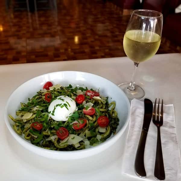 Basil pesto bucatini in a bowl with a glass of wine on a table