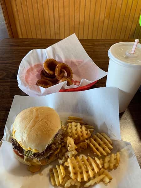 Loaded burger with cheese and fries, and a plate of onion rings with a drink
