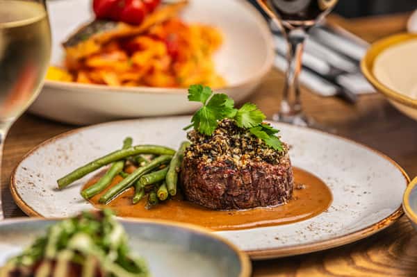 Beef filet topped with seasoned crumbs and herbs, served with green beans and sauce in an upscale dining setting.