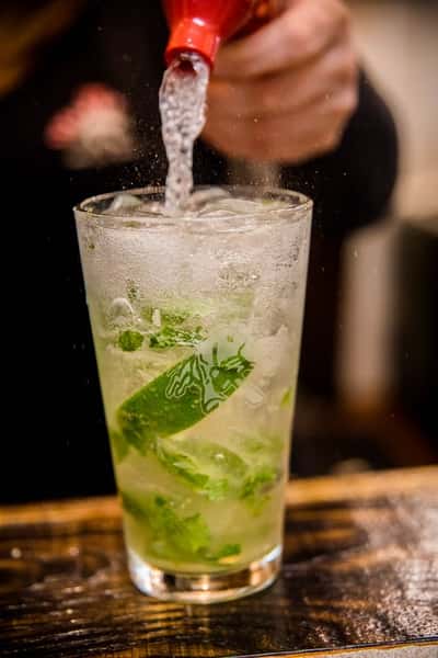 A refreshing mojito with mint leaves and lime, topped with sparkling soda, being freshly poured for a crisp and vibrant presentation.