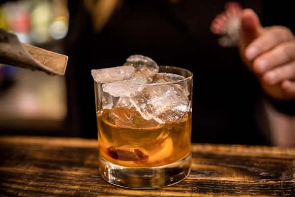 A classic whiskey cocktail served over ice in a short glass, garnished with an orange peel, creating a warm and sophisticated bar ambiance.