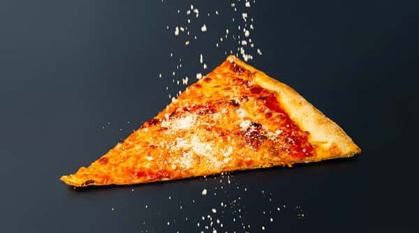 Hand in black glove holding a cheese pizza slice with parmesan falling on it against a dark background.