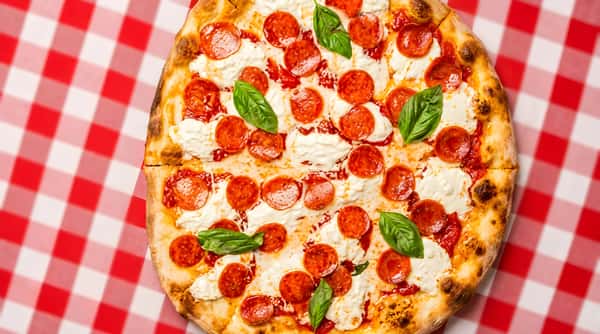 Pepperoni pizza with basil and melted mozzarella on a red and white checkered tablecloth.