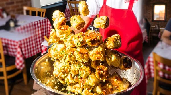 Garlic knots, stacked high on a metal skewer with some falling into a bowl.