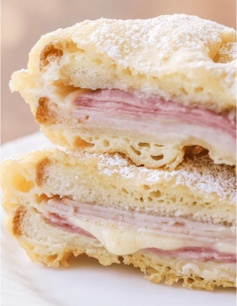 This image shows a **Monte Cristo sandwich**, which is a deep-fried or pan-fried ham and cheese sandwich, often dusted with powdered sugar. It's a rich, savory-sweet dish typically made with layers of ham, turkey, and Swiss cheese between slices of soft bread, then battered and fried.