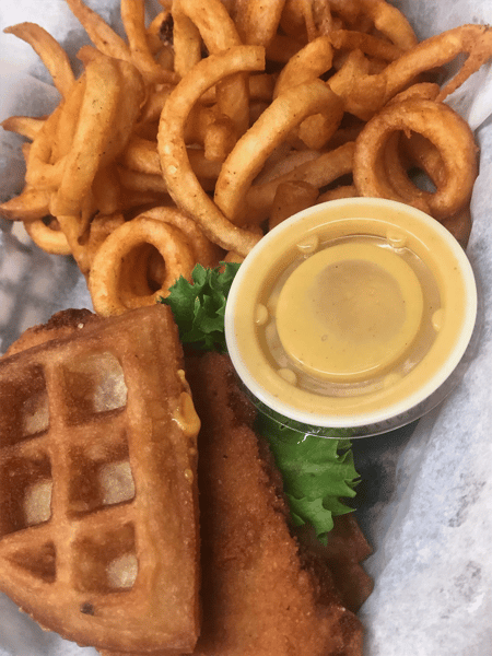 Crispy waffle sandwich with melted cheese, curly fries, lettuce, and a side of honey mustard dipping sauce.