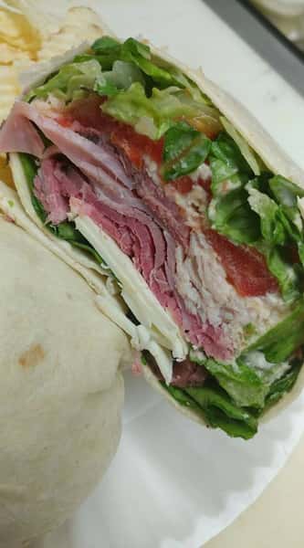 A hearty wrap filled with layers of deli meats, shredded lettuce, sliced tomatoes, and cheese, all tightly rolled in a flour tortilla.