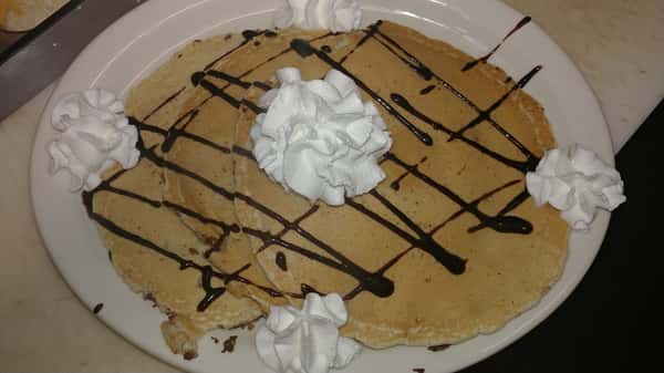 Chocolate-drizzled pancakes topped with dollops of whipped cream on a white plate.