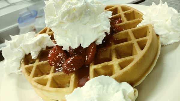 Golden waffle topped with sweet strawberries and a generous amount of whipped cream in the center and around the sides.