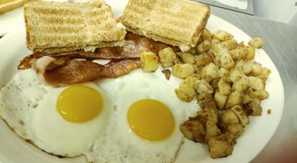 Classic breakfast plate with sunny-side-up eggs, crispy bacon, toast, and seasoned diced potatoes.