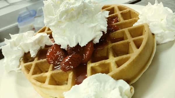 Golden waffles topped with strawberry sauce and whipped cream, served on a white plate.