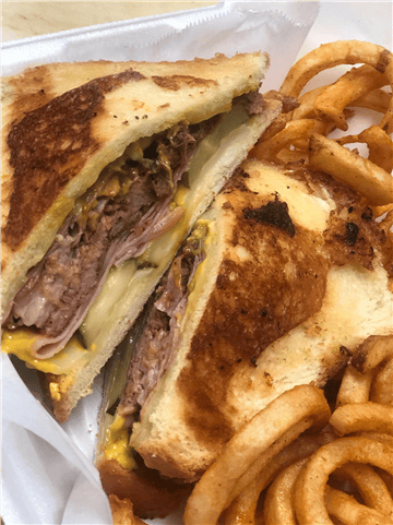 Pressed Cuban sandwich with layers of meat, pickles, and mustard, served with seasoned curly fries.