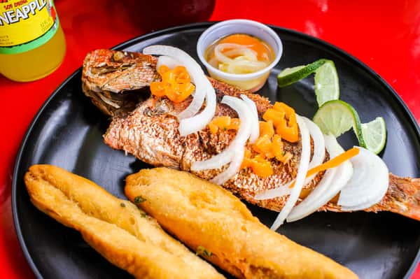 Hearty dish of rice and beans, fried plantains, and grilled fish, accompanied by colorful vegetables.