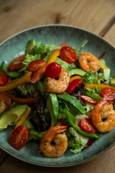 Grilled shrimp salad with fresh mixed greens, avocado, cherry tomatoes, and sliced peppers, served as a vibrant, healthy seafood restaurant dish.