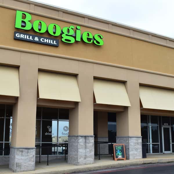 Boogies Grill & Chill restaurant exterior with bright green signage, beige stucco facade, and shaded patio seating—casual American grill and bar offering drinks and comfort food in a relaxed dining atmosphere.