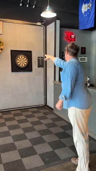 Guest playing darts inside Boogies Grill & Chill with wall-mounted dartboard, checkered flooring, and casual sports bar atmosphere—fun nightlife and bar games.