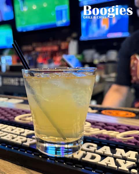 Chilled yellow cocktail on ice with black straw at Boogies Grill & Chill bar—craft drink served in a lively sports bar setting with TVs and game-day vibe.