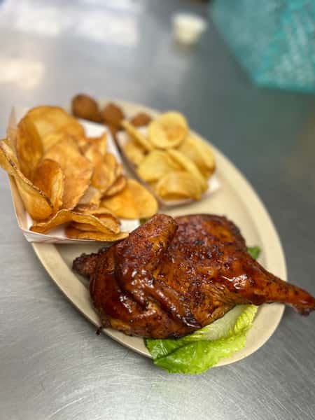 Grilled half chicken coated in sweet and tangy barbecue sauce, paired with thick-cut potato chips and crispy hushpuppies, presented on a diner-style platter.