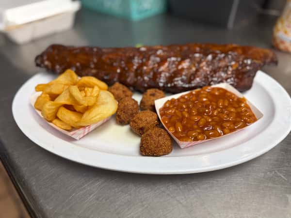 Barbecue pork ribs glazed in smoky BBQ sauce, served with crispy potato chips, baked beans, and golden hushpuppies on a white plate — classic Southern BBQ platter.