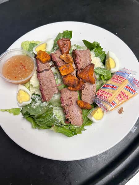 Fresh chopped romaine salad topped with sliced smoked brisket, croutons, hard-boiled eggs, parmesan cheese, and Captain's Wafers crackers, served with a vinaigrette dressing.
