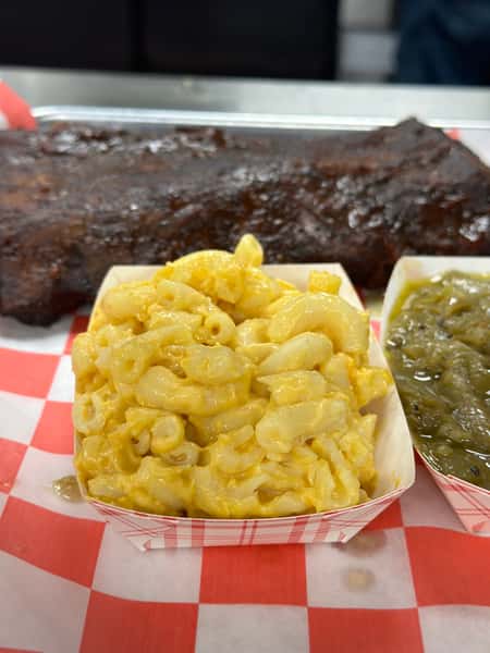Creamy baked mac and cheese served alongside slow-smoked pork ribs and seasoned green beans, plated on a red checkered tray.