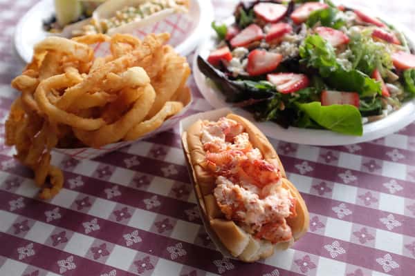 lobster roll with a side of onion rings and a strawberry salad