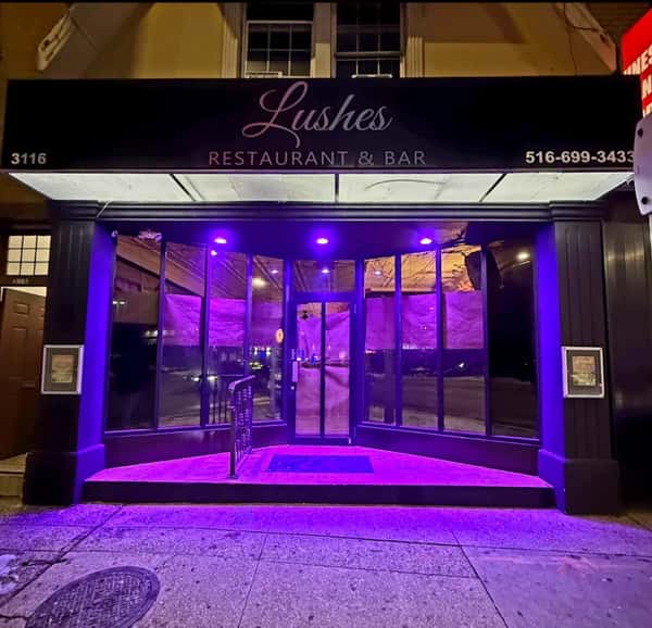 Exterior of Lushes Restaurant & Bar in Oceanside, NY, illuminated with purple lighting at night, featuring a modern glass entrance and upscale nightlife ambiance.