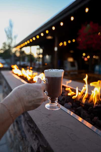 Woman enjoying a cocktail at the bar inside Otto's Landing, with views of the patio and evening light streaming through garage-style windows.