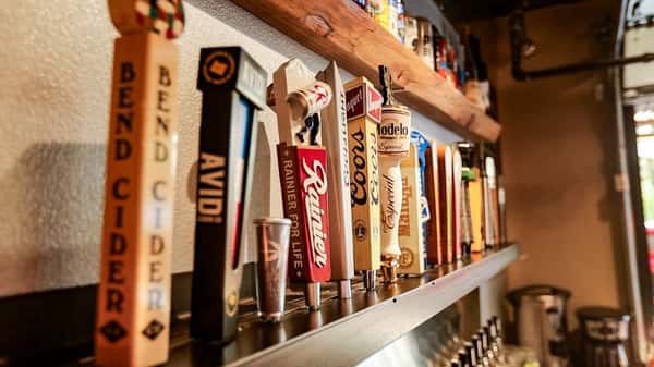 Close-up row of beer taps at Otto's Landing featuring Bend Cider, Rainier, Modelo, Coors, and more, showcasing a wide draft selection.