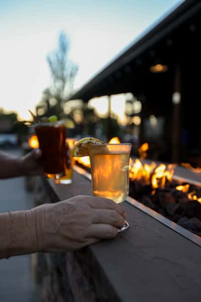 Close-up of a guest holding a steaming hot toddy with lemon garnish near the outdoor fire pit at Otto's Landing, capturing cozy evening vibes.