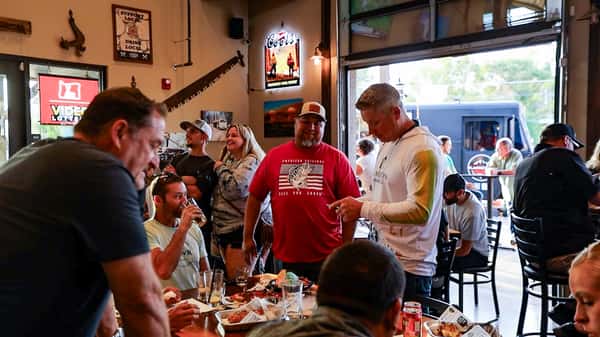 Lively indoor dining scene at a rustic American bar and grill, with groups of people enjoying food, drinks, and conversation in a casual, welcoming atmosphere.