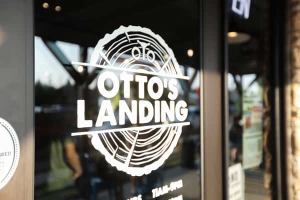 Close-up of the Otto's Landing restaurant logo displayed on a glass door, featuring a tree-ring design that evokes a rustic, woodsy vibe at this casual dining spot.