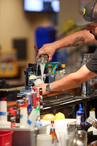 Bartender pouring a fresh cocktail at Otto's Landing bar, surrounded by bottles and garnishes, showcasing handcrafted drink service.