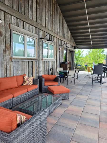 Cozy covered patio at Otto's Landing featuring wicker lounge seating with burnt orange cushions, rustic wood siding, and outdoor dining tables—perfect for relaxed gatherings in a shaded outdoor setting.